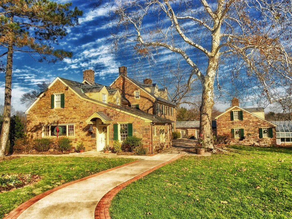 A house surrounded by trees displaying autumn foliage, with a sidewalk in the foreground.