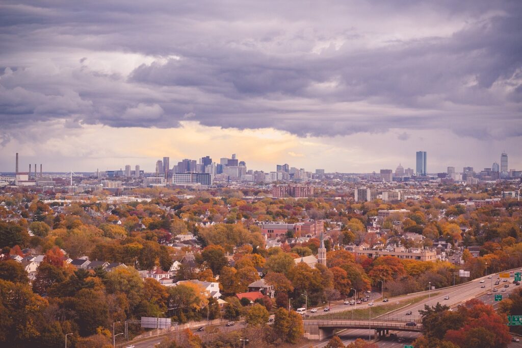 A house surrounded by trees with autumn foliage beneath a cloudy sky in an urban landscape.