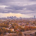 A house surrounded by trees with autumn foliage beneath a cloudy sky in an urban landscape.